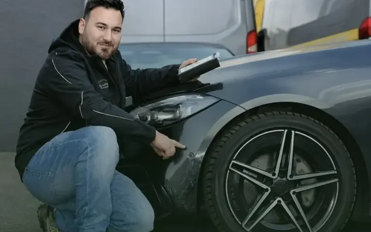 Kfz-Gutachter zeigt einen Unfallschaden am Kotflügel eines dunklen Autos
